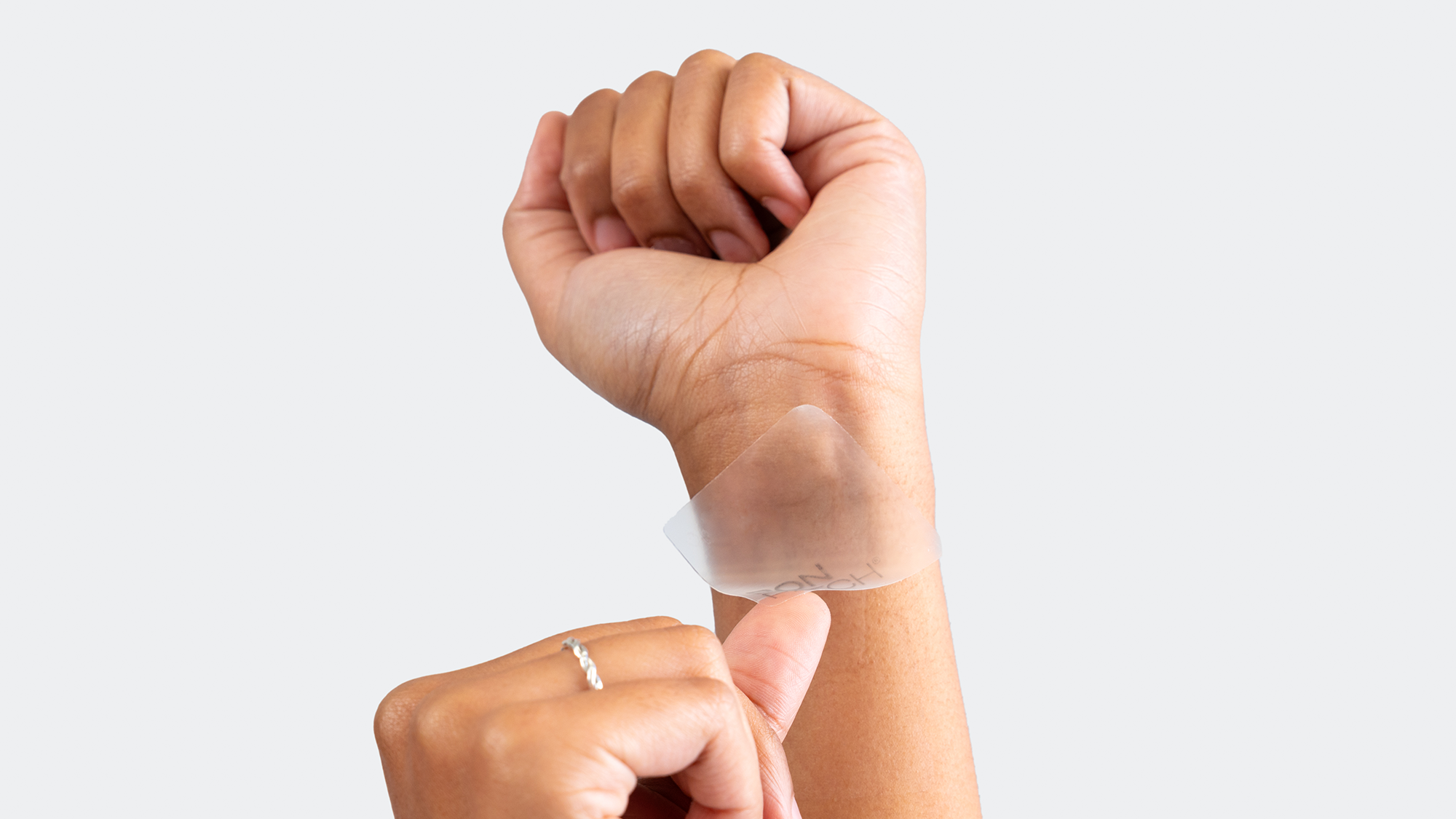 Hand applying a clear adhesive patch on another hand against a white background